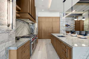 Kitchen featuring brown cabinetry, light stone counters, double oven range, premium range hood, and a large island
