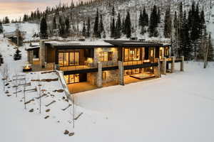 Snow covered property with stone siding, a patio area, a standing seam roof, and a metal roof