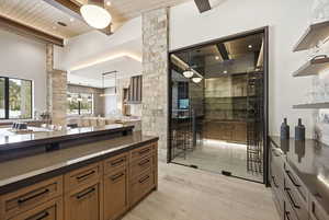 Bar area featuring open shelves, a wooden ceiling with exposed beams, decorative light fixtures, a high ceiling, and dark stone counters