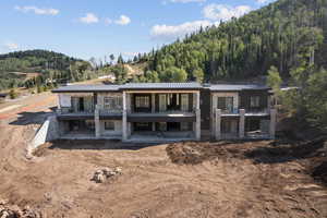 Rear view of property featuring stone siding, a standing seam roof, a metal roof, a balcony, and a view of trees