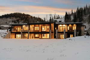 Snow covered rear of property with a balcony and stone siding