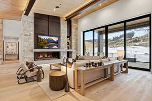 Living area with a fireplace, light wood-type flooring, a wooden ceiling with exposed beams, and a high ceiling