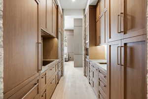 Kitchen with black electric stovetop, stainless steel oven, and light wood finished floors