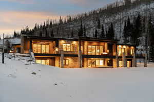 Snow covered rear of property with a balcony and stone siding