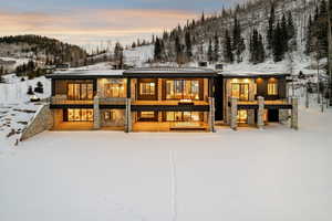 Snow covered rear of property with stone siding, a patio area, and a balcony