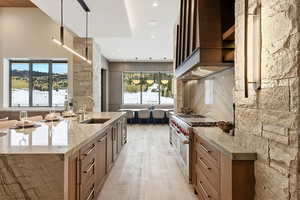 Kitchen with light stone counters, healthy amount of natural light, pendant lighting, custom range hood, and recessed lighting