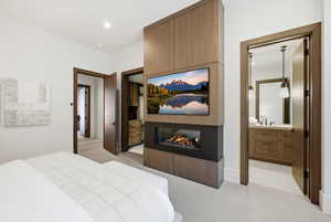 Bedroom with light carpet, a multi sided fireplace, and ensuite bathroom