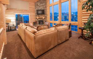 Carpeted living area featuring log walls, high vaulted ceiling, and a fireplace