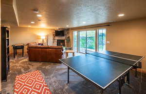 Playroom with a textured ceiling, dark colored carpet, a stone fireplace, and recessed lighting