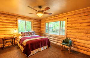 Carpeted bedroom with a textured ceiling, a ceiling fan, and rustic walls