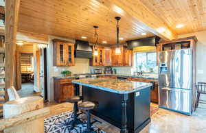 Kitchen featuring glass insert cabinets, appliances with stainless steel finishes, a kitchen bar, a kitchen island, and brown cabinetry