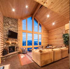 Carpeted living room featuring high vaulted ceiling, log walls, a wooden ceiling with exposed beams, a stone fireplace, and a sauna