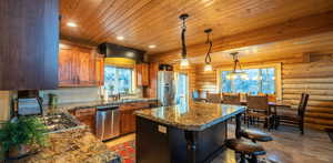 Kitchen featuring plenty of natural light, decorative light fixtures, brown cabinetry, stainless steel appliances, and wooden ceiling
