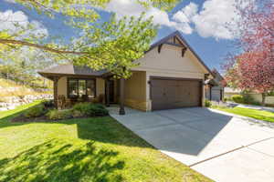 View of front of property featuring a front lawn, driveway, a garage, and stone siding
