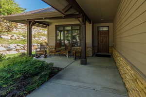 View of exterior entry featuring covered porch, stone siding, and roof with shingles