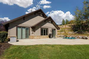 Rear view of property with a patio, a lawn, stone siding, and an outdoor pool
