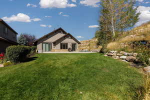 Rear view of property with a patio, a lawn, and stone siding