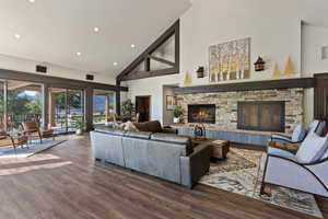 Living room featuring high vaulted ceiling, wood finished floors, recessed lighting, and a stone fireplace