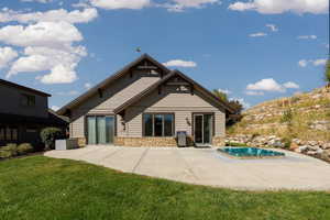 Rear view of house featuring stone siding, a patio, an outdoor pool, and a yard