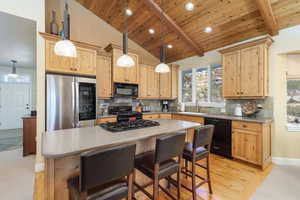 Kitchen featuring light brown cabinetry, backsplash, black appliances, a breakfast bar area, and a center island
