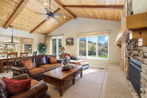 Living room with a wood ceiling with exposed beams, high vaulted ceiling, a fireplace, a chandelier, and a ceiling fan