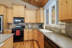 Kitchen featuring light brown cabinets, black appliances, tasteful backsplash, lofted ceiling, and light wood-style flooring