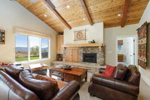 Living area featuring a wooden ceiling with exposed beams, a stone fireplace, high vaulted ceiling, and a mountain view
