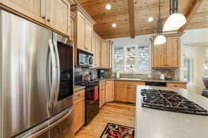 Kitchen featuring black appliances, backsplash, light wood finished floors, decorative light fixtures, and a wooden ceiling with exposed beams