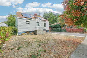 Back of house with solar panels, a chimney, and roof with shingles