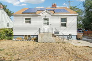 Rear view of property featuring solar panels, a chimney, and a shingled roof
