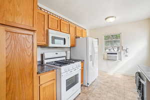 Kitchen featuring white appliances, dark countertops, light tile patterned flooring, and cooling unit