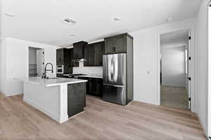 Kitchen featuring stainless steel appliances, a kitchen island with sink, light wood-style flooring, light stone countertops, and under cabinet range hood