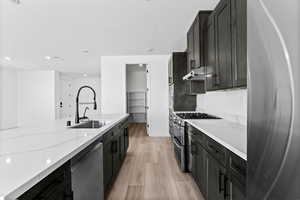Kitchen featuring dark cabinetry, light wood-type flooring, stainless steel appliances, light stone counters, and recessed lighting