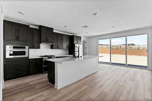 Kitchen featuring stainless steel appliances, a kitchen island with sink, light wood finished floors, recessed lighting, and light stone counters