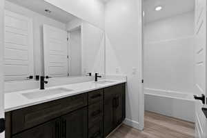 Full bathroom featuring double vanity, light wood-style floors, and shower / tub combination