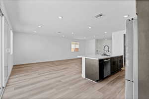 Kitchen with light wood-style floors, open floor plan, a center island with sink, appliances with stainless steel finishes, and recessed lighting