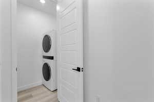Laundry area with light wood-style flooring, stacked washer and clothes dryer, and recessed lighting
