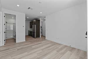 Unfurnished living room featuring light wood-style flooring, stacked washing machine and dryer, and recessed lighting