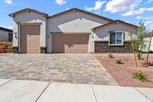 Mediterranean / spanish-style house featuring a garage, decorative driveway, stone siding, stucco siding, and a tile roof