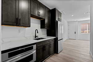 Kitchen featuring light stone counters, stainless steel oven, light wood finished floors, and recessed lighting