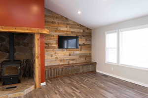 Living room with wooden walls, a wood stove, LVP wood finished floors, vaulted ceiling, and recessed lighting