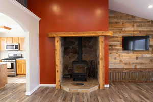 Living room with a wood stove, LVP wood finished floors, arched walkways, wood walls, and lofted ceiling