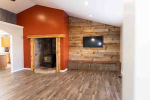 Living room with a wood stove, wood LVP finished floors, arched walkways, and high vaulted ceiling