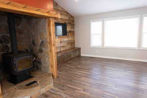 Living room with wood walls, a wood stove, LVP wood finished floors, plenty of natural light, and vaulted ceiling