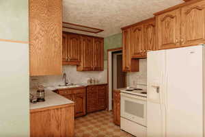 Kitchen featuring white appliances, light countertops, oak cabinets, backsplash, and light flooring