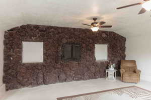 Finished bonus room featuring textured ceiling, finished concrete floors, ceiling fans, rock wall
