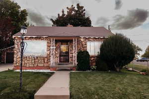 View of front of property featuring stone siding, a garage, a front lawn, a chimney, and roof with shingles