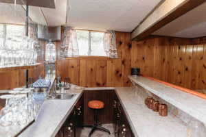 Wet bar with sink, wooden walls, light countertops, a textured ceiling, and beam