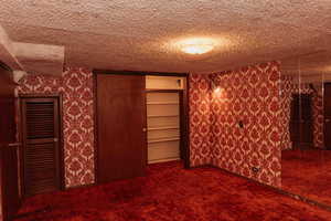 Bedroom with dark colored carpet, wallpapered walls, a textured ceiling, and a large closet