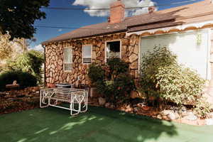 Rear view of property with a chimney, stone siding, and roof with shingles